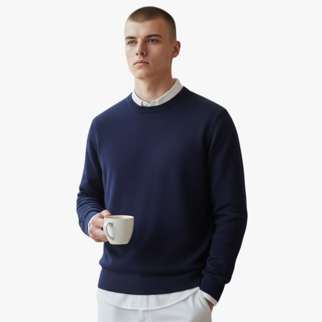 Man wearing a navy sweater over a white shirt, holding a cup against a plain background