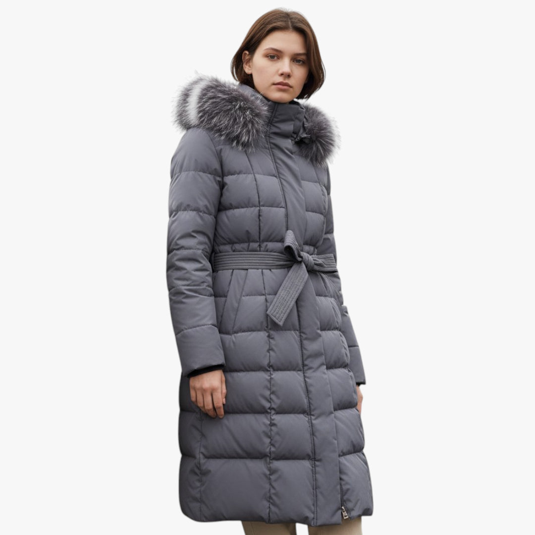 Woman wearing a long gray puffer coat with a fur hood on a white background