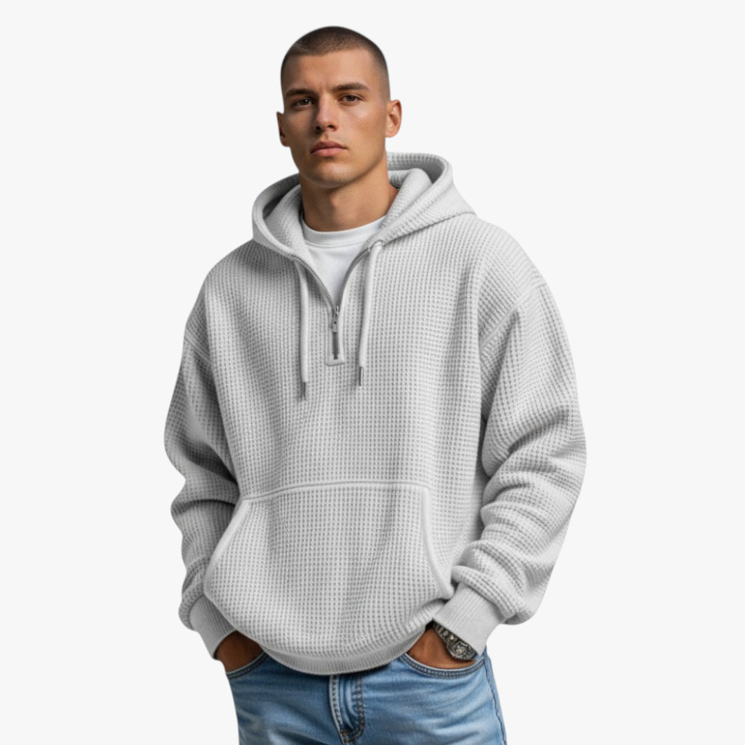 Man wearing a gray hoodie and light blue jeans on a white background