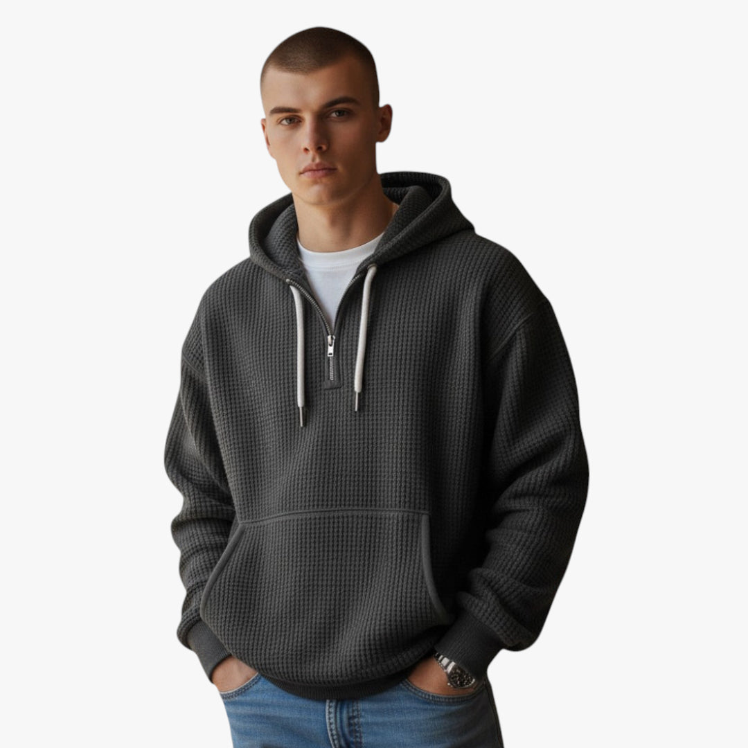 Man wearing a dark gray waffle-textured hoodie with a zipper on a white background