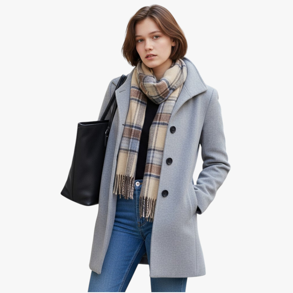 Woman wearing a gray coat, plaid scarf, and blue jeans on a white background